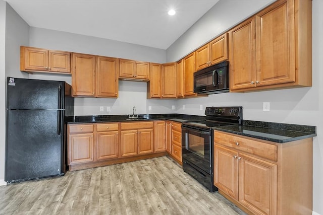 kitchen featuring light wood-style floors, brown cabinetry, a sink, dark stone counters, and black appliances