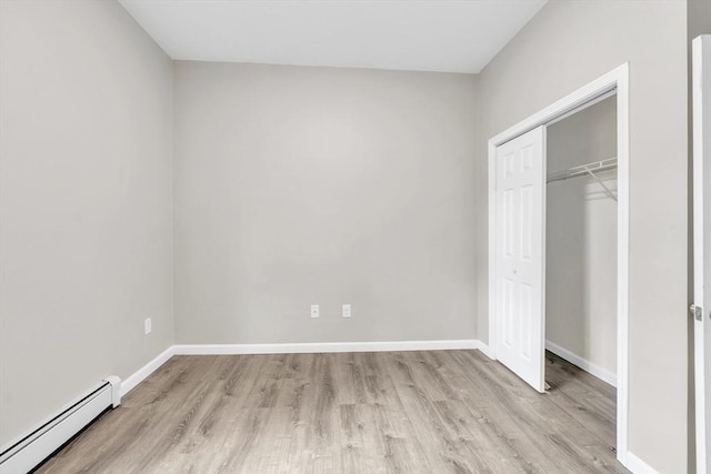 unfurnished bedroom with baseboards, a closet, a baseboard radiator, and light wood-style floors