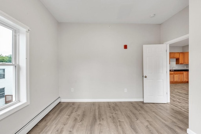 spare room with baseboard heating, light wood-style flooring, and baseboards