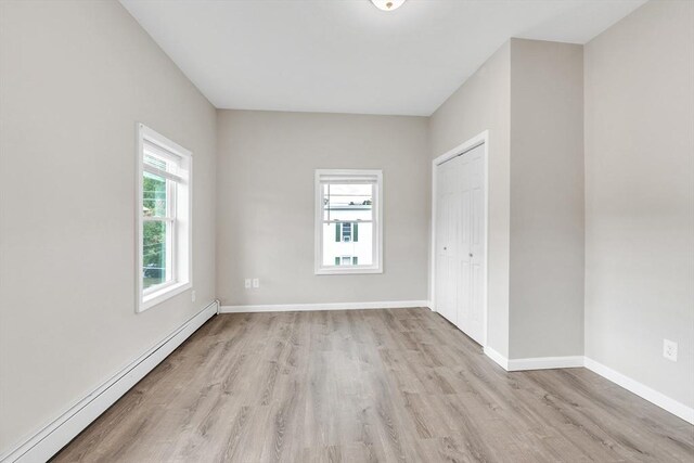 unfurnished bedroom with a baseboard heating unit, a closet, baseboards, and light wood-style floors