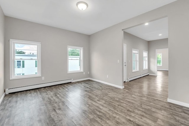 empty room featuring a baseboard heating unit, a baseboard radiator, baseboards, and wood finished floors