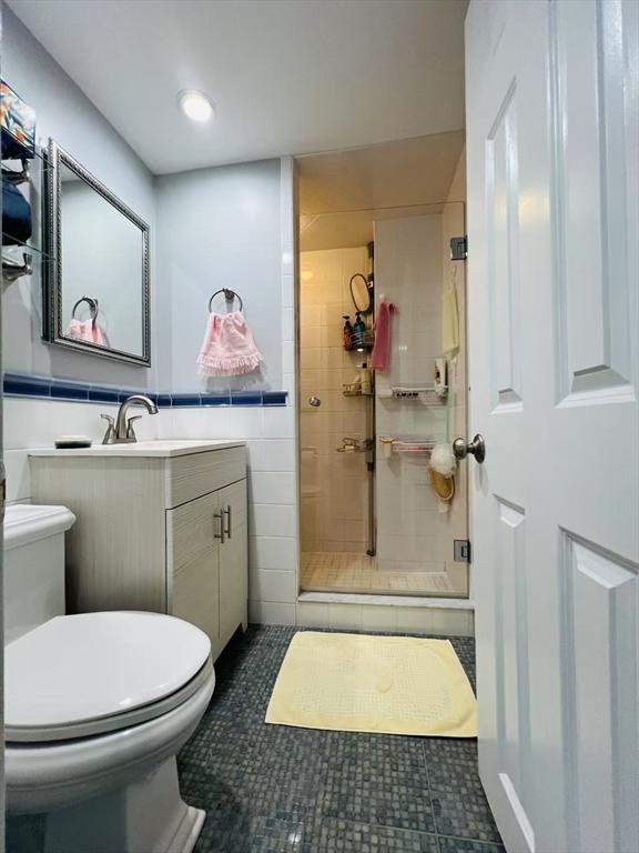 full bath with tile walls, tile patterned flooring, a stall shower, vanity, and toilet