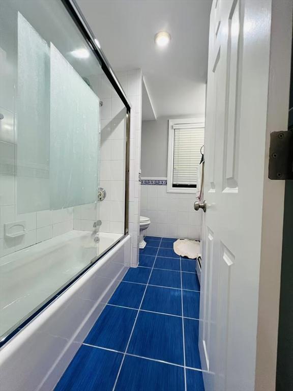 full bathroom featuring bath / shower combo with glass door, tile patterned floors, toilet, and tile walls