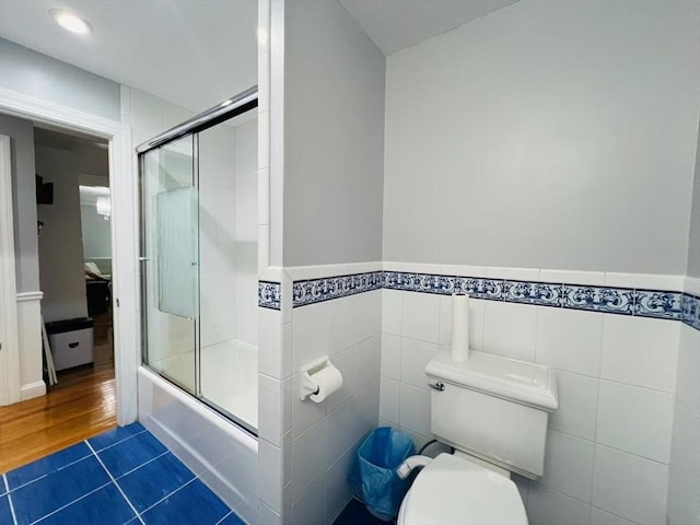 full bath with shower / bath combination with glass door, toilet, tile patterned floors, and a wainscoted wall