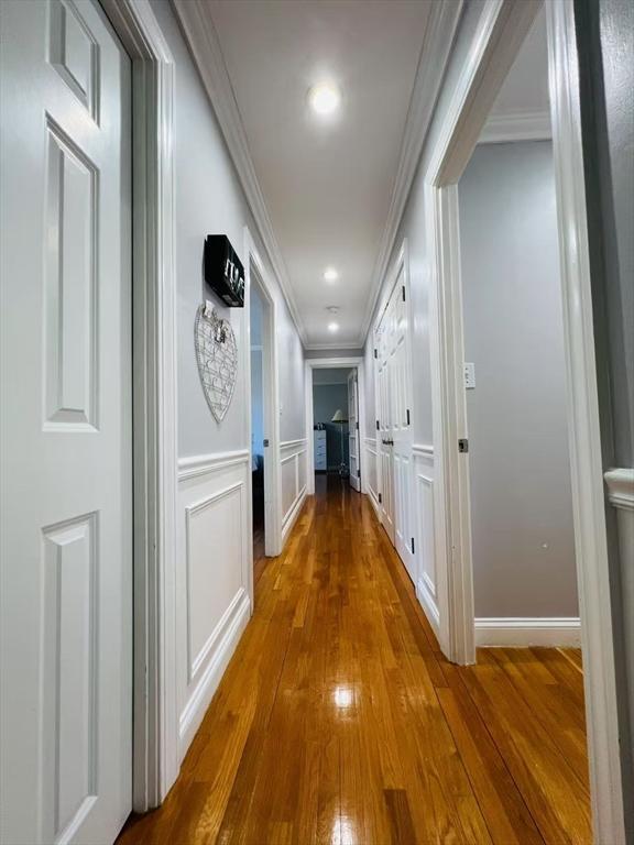 corridor featuring a wainscoted wall, ornamental molding, a decorative wall, and hardwood / wood-style floors