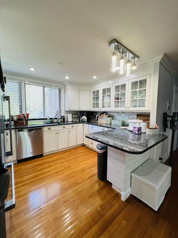 kitchen featuring tasteful backsplash, stainless steel dishwasher, a sink, white cabinets, and ornamental molding