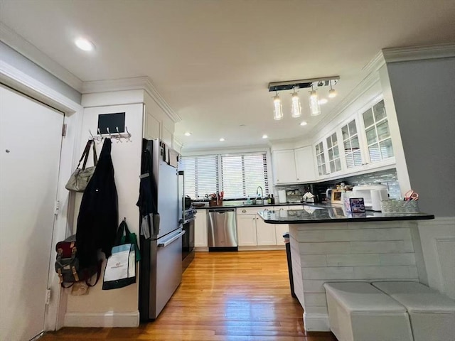 kitchen with dark countertops, appliances with stainless steel finishes, light wood-type flooring, glass insert cabinets, and white cabinetry