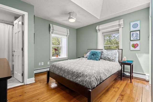 bedroom with baseboard heating, hardwood / wood-style floors, baseboards, and a ceiling fan