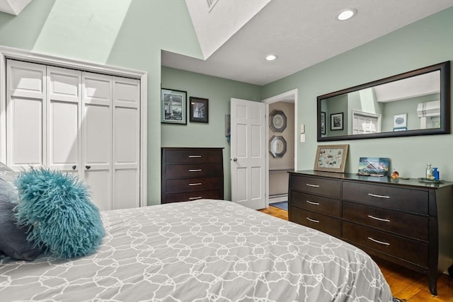 bedroom with wood finished floors, a closet, recessed lighting, and a baseboard heating unit