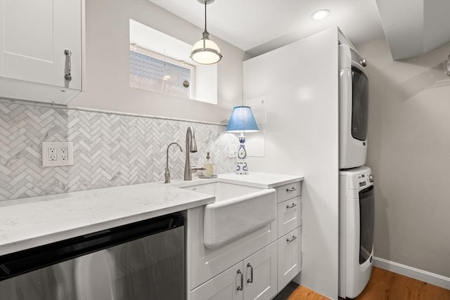 kitchen with estacked washer and dryer, stainless steel dishwasher, light wood-style floors, decorative backsplash, and a sink