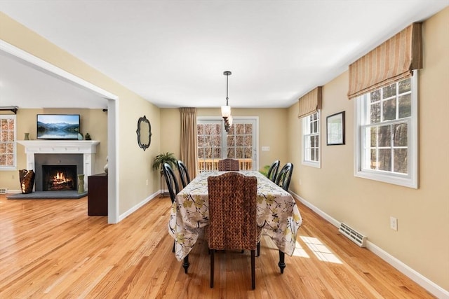 dining room with baseboards, a lit fireplace, light wood-type flooring, and visible vents