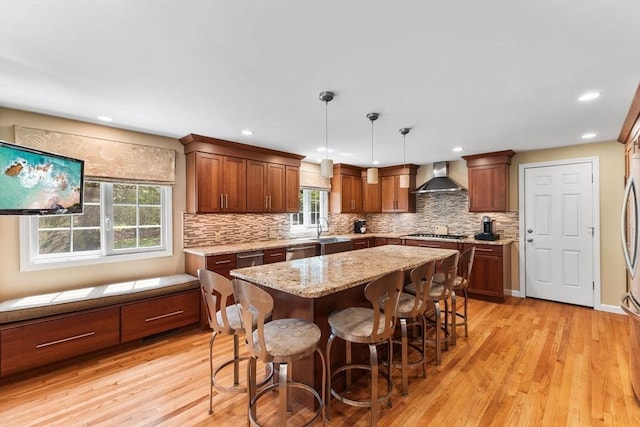 kitchen featuring wall chimney range hood, plenty of natural light, tasteful backsplash, and a sink