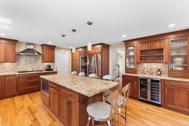 kitchen with decorative backsplash, wine cooler, wall chimney range hood, a kitchen bar, and appliances with stainless steel finishes