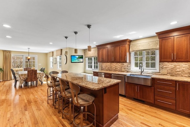 kitchen featuring a sink, light wood finished floors, dishwasher, a kitchen breakfast bar, and a center island