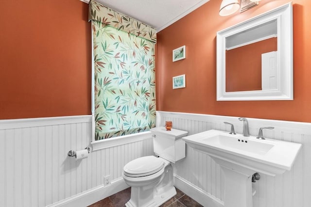 half bath featuring crown molding, tile patterned floors, wainscoting, and toilet