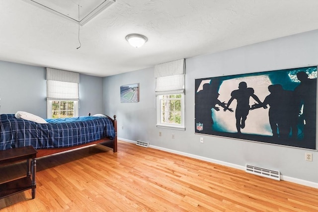 bedroom with visible vents, multiple windows, wood finished floors, and attic access