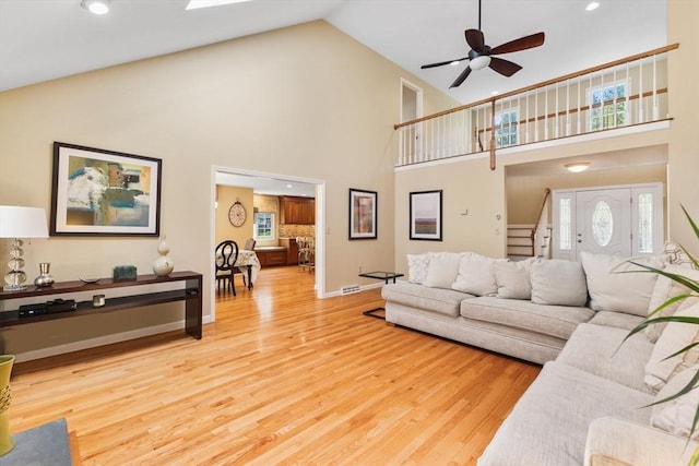 living room with high vaulted ceiling, light wood-type flooring, and stairs