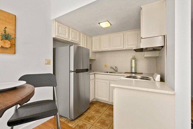kitchen with a sink, light countertops, wall chimney exhaust hood, electric stove, and freestanding refrigerator