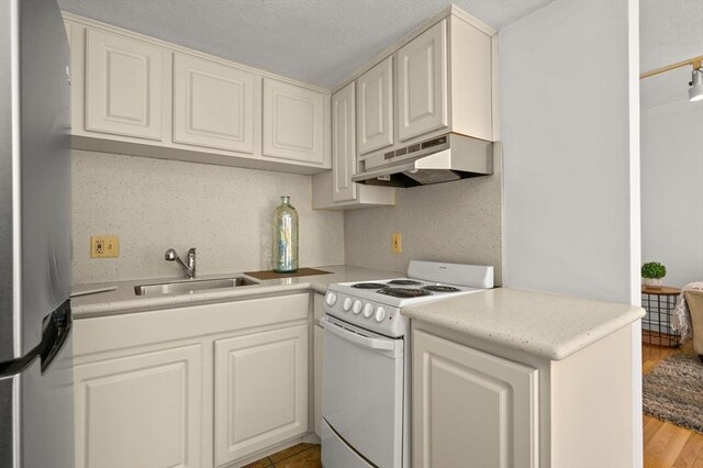 kitchen with white electric range, a sink, light countertops, freestanding refrigerator, and under cabinet range hood