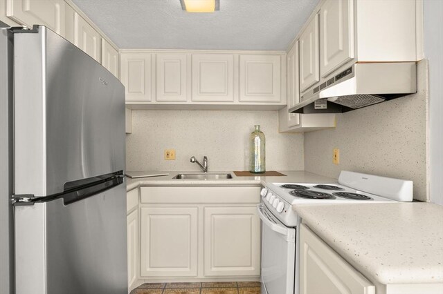kitchen with a sink, light countertops, electric stove, freestanding refrigerator, and under cabinet range hood