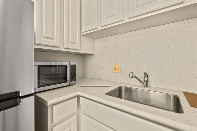kitchen with backsplash, a sink, light countertops, stainless steel appliances, and white cabinetry