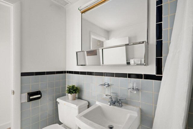 bathroom featuring a sink, toilet, and tile walls