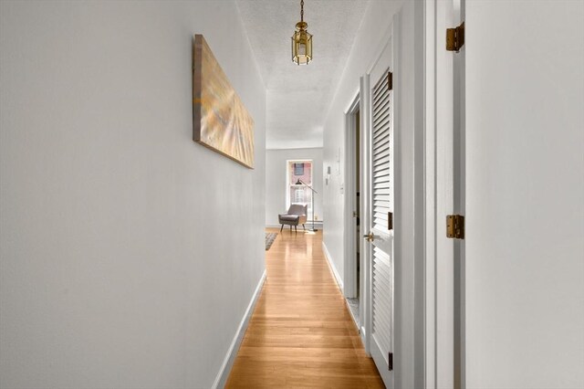 hallway featuring baseboards, a textured ceiling, and light wood-type flooring