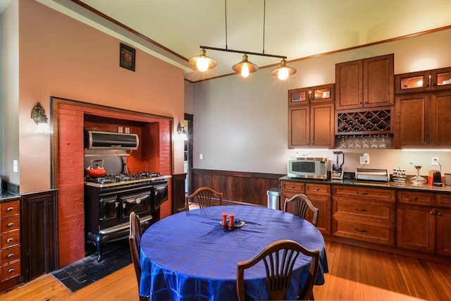 kitchen with appliances with stainless steel finishes, decorative light fixtures, dark stone countertops, crown molding, and light wood-type flooring