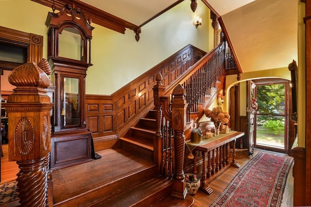 stairway featuring a high ceiling, ornamental molding, and hardwood / wood-style flooring