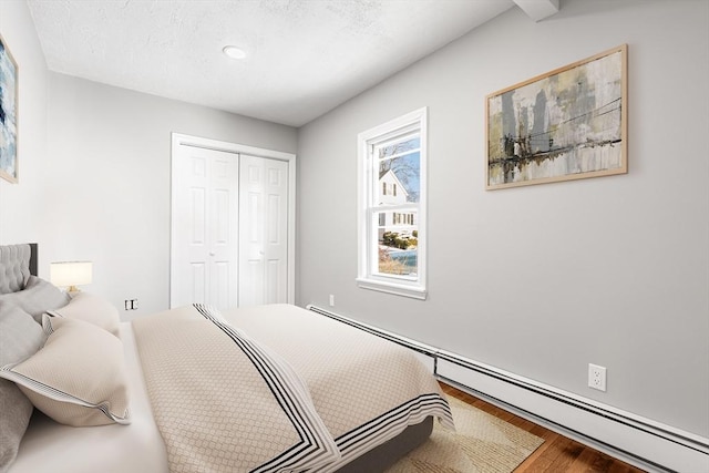 bedroom with a closet, baseboard heating, and wood finished floors