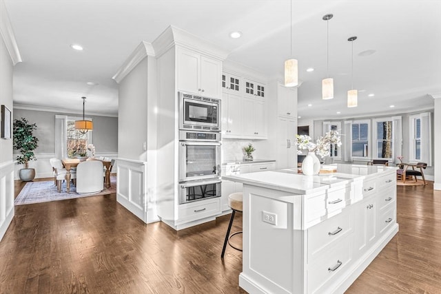 kitchen with white cabinetry, a kitchen island, pendant lighting, crown molding, and appliances with stainless steel finishes