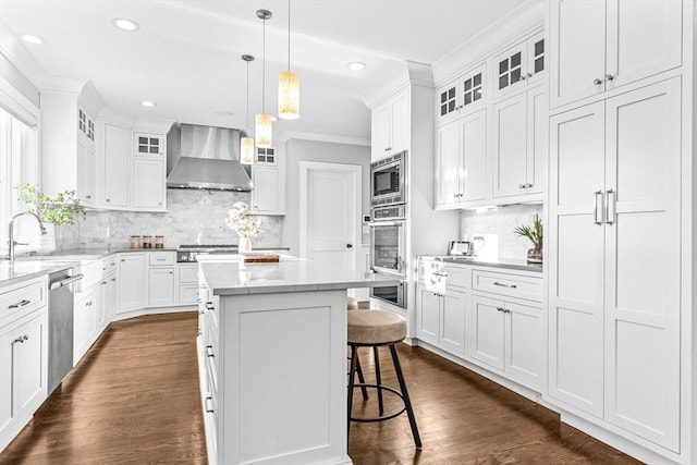 kitchen featuring stainless steel appliances, a center island, white cabinetry, wall chimney range hood, and backsplash