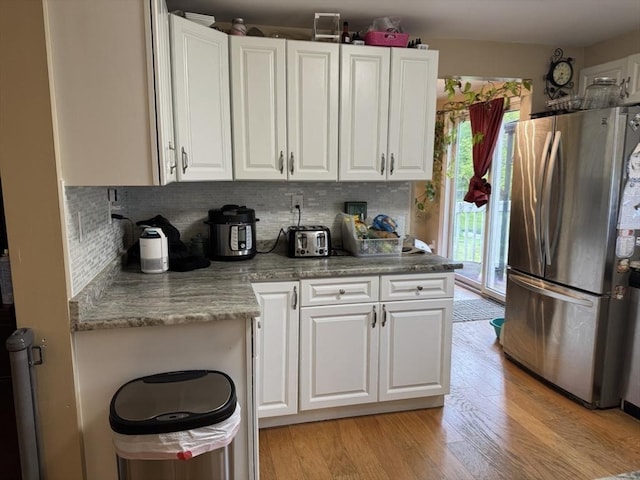 kitchen with freestanding refrigerator, white cabinets, light wood-style floors, and backsplash