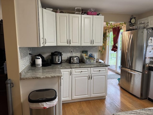 kitchen featuring freestanding refrigerator, white cabinetry, light wood-type flooring, backsplash, and light countertops