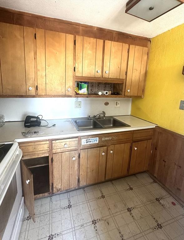 kitchen featuring light floors, brown cabinetry, light countertops, a sink, and white electric range oven