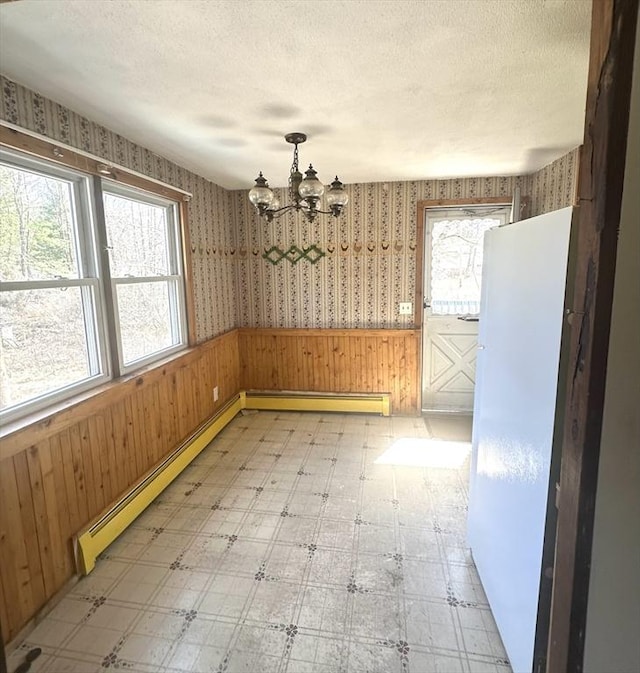 unfurnished dining area featuring light floors, a chandelier, and a baseboard heating unit