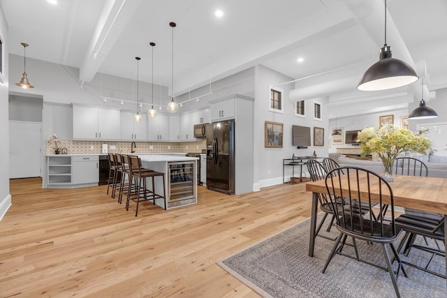 dining space with beam ceiling, light wood finished floors, recessed lighting, beverage cooler, and baseboards