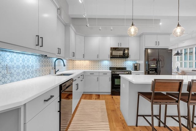 kitchen with a breakfast bar, tasteful backsplash, a sink, light wood-type flooring, and black appliances