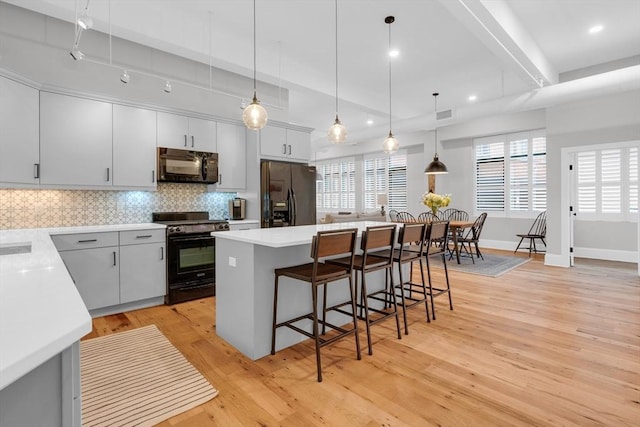 kitchen featuring decorative backsplash, a breakfast bar area, a center island, light wood-type flooring, and black appliances