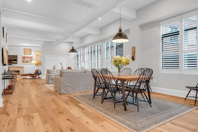 dining area featuring a fireplace, beamed ceiling, baseboards, and wood finished floors