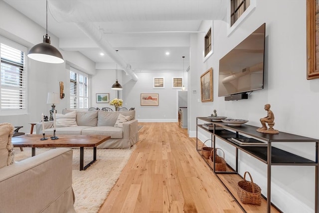 living area with beam ceiling, light wood-style flooring, and baseboards