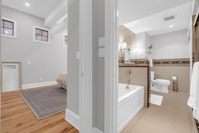 full bath with visible vents, toilet, wood finished floors, a garden tub, and tile walls