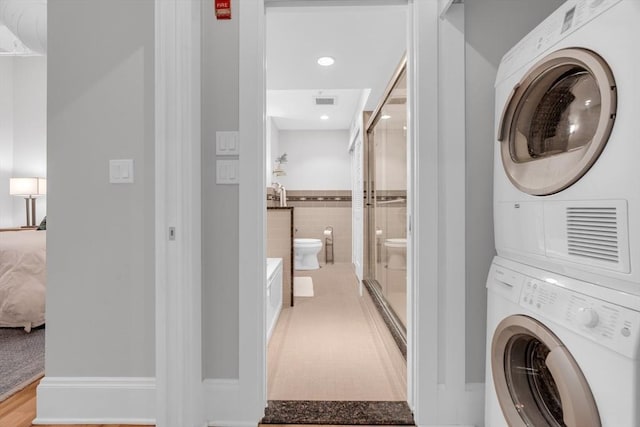 washroom with laundry area, light wood-style flooring, tile walls, and stacked washer and clothes dryer