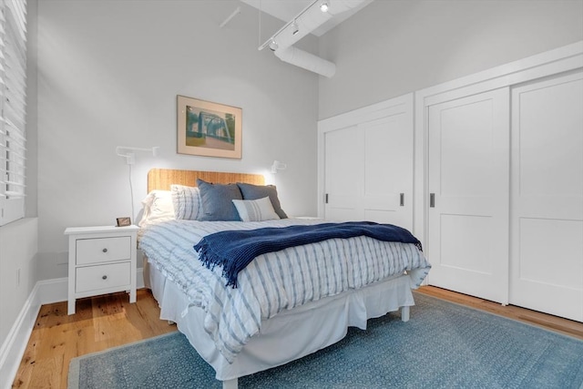 bedroom featuring multiple closets, rail lighting, a high ceiling, light wood-type flooring, and baseboards