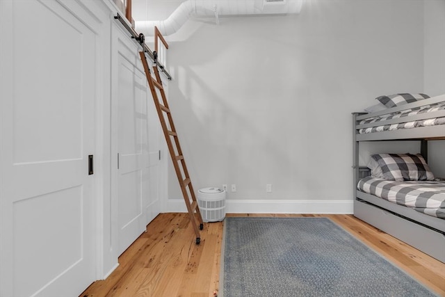 bedroom featuring light wood finished floors, a barn door, and baseboards