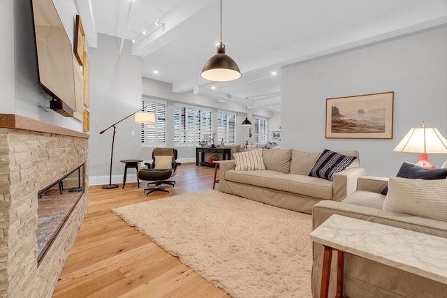 living area featuring beam ceiling, recessed lighting, light wood-style flooring, a stone fireplace, and baseboards