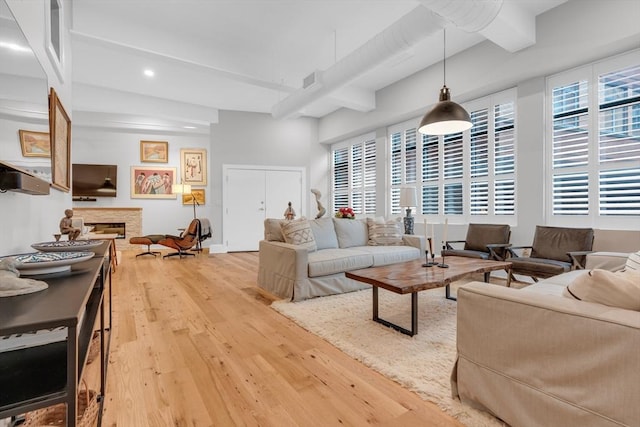 living room featuring plenty of natural light, light wood-style flooring, a fireplace, and beamed ceiling