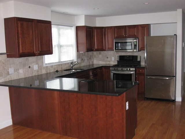 kitchen featuring tasteful backsplash, a sink, stainless steel appliances, dark wood-style flooring, and a peninsula