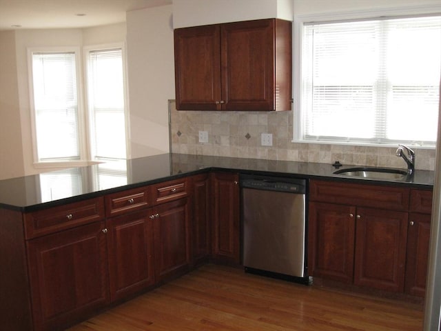 kitchen featuring stainless steel dishwasher, a sink, dark countertops, wood finished floors, and a peninsula