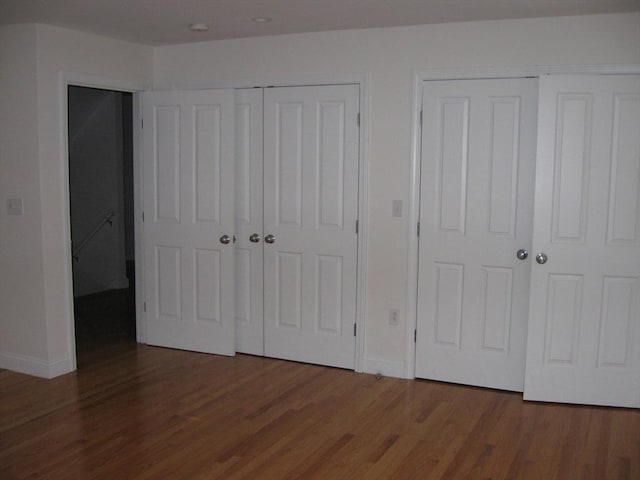 unfurnished bedroom featuring wood finished floors, two closets, and baseboards